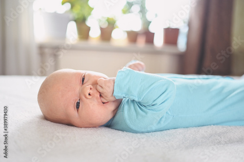 Cute emotional funny newborn infant crying boy laying on bed. Infant baby facial expressions.