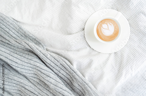 Cup of cappuccino coffee in morning bed. Cozy autumn or winter flatlay top view. Copy space. Concept minimalism.