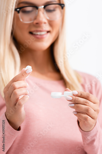Cap and container with contact lenses in hands of smiling woman in eyeglasses on blurred foreground isolated on white
