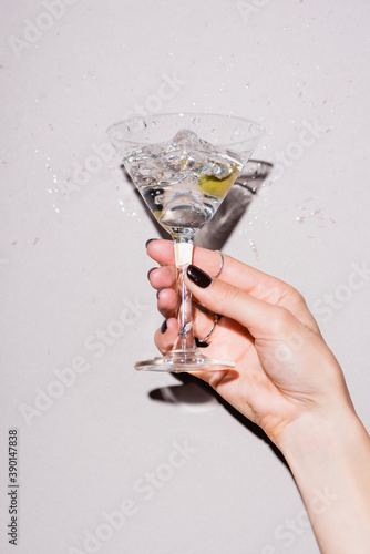 cropped view of woman shaking glass of martini with olive near drops of alcohol on white