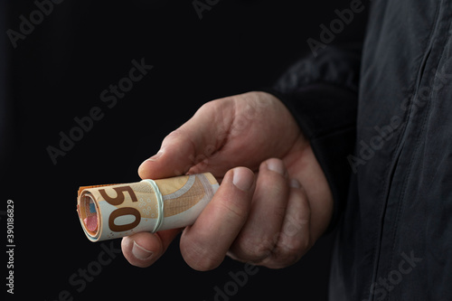 Close up of male hand offering cash on black background. Illegal smuggling concept.