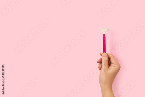 Mano femenina sosteniendo una maquinilla de afeitar sobre un fondo rosa pastel liso y aislado. Vista de frente y de cerca. Copy space