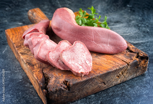 Traditional cooked veal tongue with parsley offered as close-up on a rustic wooden board