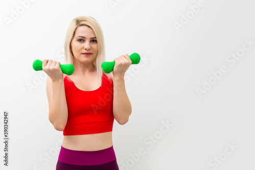 Athletic woman pumping up muscles with dumbbells on gray background