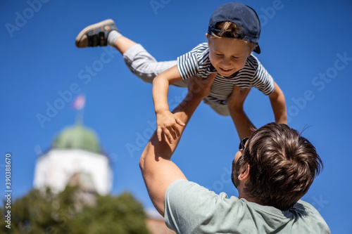 Young father throws up his cute and little son in the air in front of castle. Kid is squinting and smiling