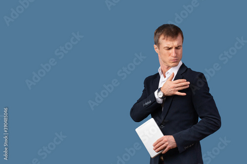 An arrogant male businessman in a suit shakes the dust off his clothes and shoulder with contempt. Studio shot on a blue background.
