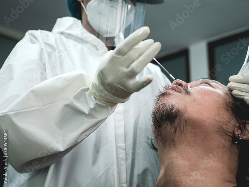 An unidentifiable nurse start to insert a long q-tip into a patient's nose for a nasopharyngeal swab rapid test. Actual prcedure done inside a clinic for company protocol.