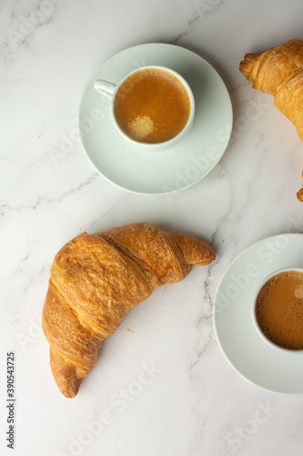 two white cups with black coffee and croissants top view.