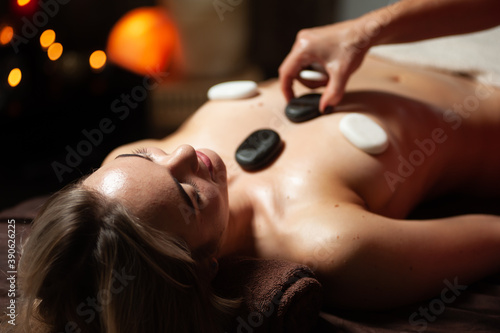 Masseur placing stones on woman's back in spa salon. Girl enjoying body treatment