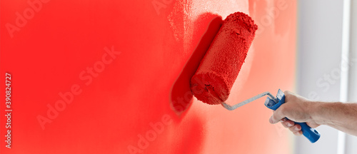 Male hand painting wall with paint roller. Painting apartment, renovating with red color paint