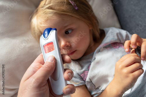 Parent takes temperature for her child with infrared thermometer at home, high fever