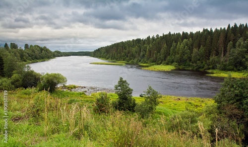 Turning Onega river with quick stream surrounded with thick green forest in summer against cloudy sky in Arkhangelsk region, Russia.