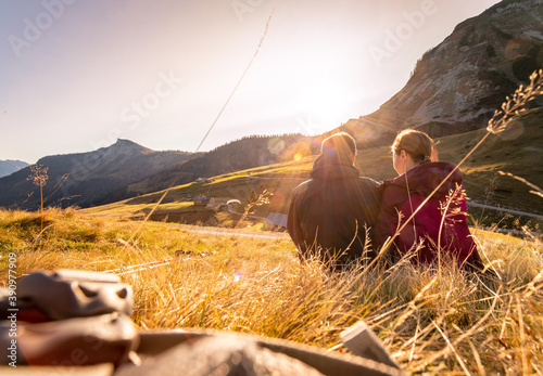 Loving couple is enjoying the sundown in the mountains, sitting on the ground. Warm colors, alps, Austria