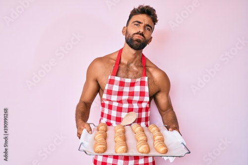 Young hispanic man shirtless wearing baker uniform holding homemade bread looking at the camera blowing a kiss being lovely and sexy. love expression.