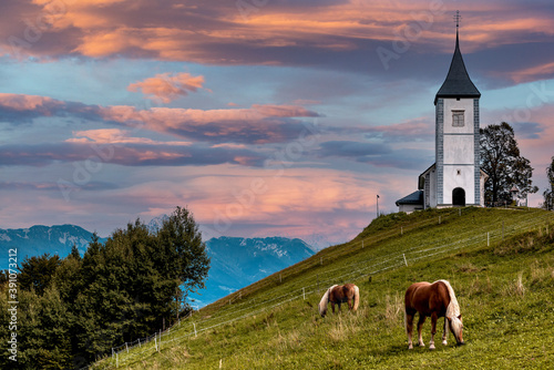 Horse Grazing at Picturesque Church Of St Primoz.in Jamnik,Kamnik, Slovenia at Sunset with Beautiful Sky