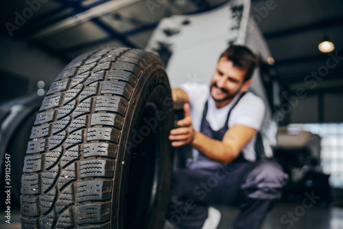 Hardworking experienced worker holding tire and he wants to change it. In background is truck. Selective focus on tire.
