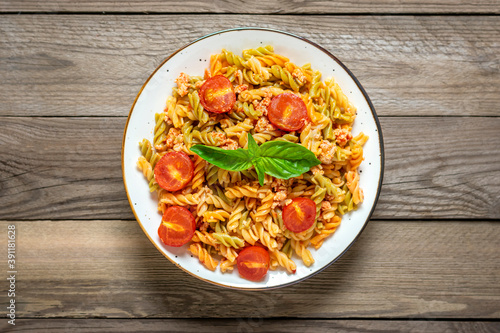 Fusilli - classic italian pasta from durum wheat with chicken meat, tomatoes cherry, basil in tomato sauce in white bowl on wooden table Mediterranean cuisine Top view Flat lay