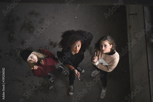 Top view of group of teenagers girl gang indoors in abandoned building, looking at camera.