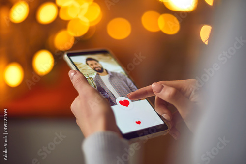 Closeup of woman looking at young man's profile photo on dating app and pressing like button