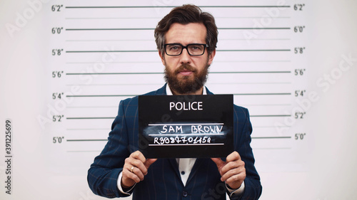 Guilty businessman in police station posing for mugshot with placard