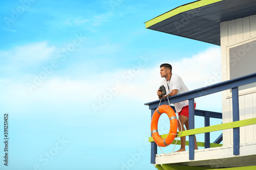 Male lifeguard with binocular on watch tower against blue sky