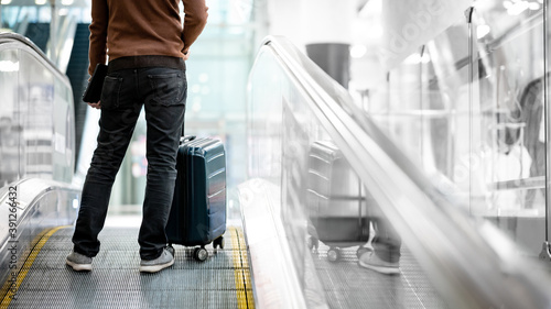 Travel insurance concept. Male tourist or passenger man carrying suitcase luggage and digital tablet on travelator or moving walkway in airport terminal.