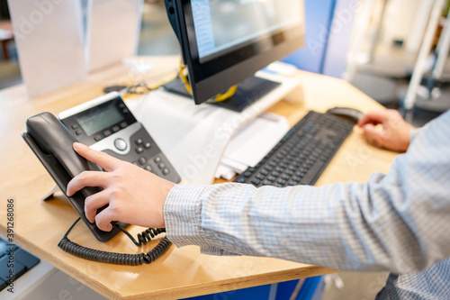 Male customer support operator hand trying to response customer call by using landline phone on working desk in office. Call center business concept