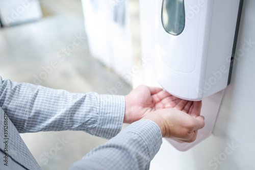 Male hands using automatic alcohol dispenser for cleaning hand in office. Infection prevention concept. Save and clean in public building.