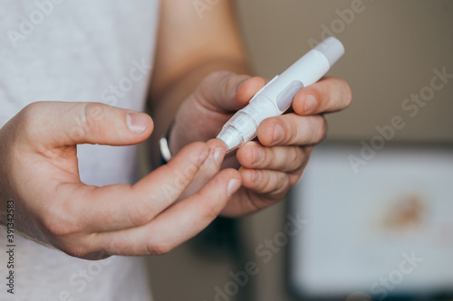 Medicine, diabetes, glycemia, healthcare and people concept - close up of a man's hands using a lancet on his finger to check blood glucose meter with copy space for text