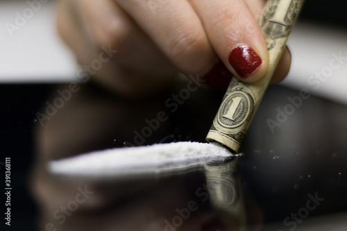 A photo of a drug addict woman, holding a rolled dollar bill with her fingers, sniffing the cocaine powder strip