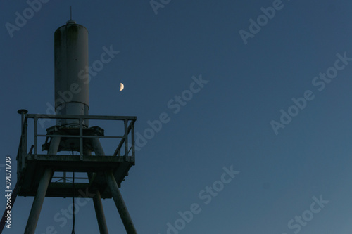 Radio beacon at twilight after sunst on blue sky with moon