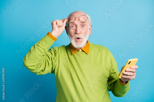 Photo of pensioner grandpa hold cellphone take off glasses wear specs green pullover isolated blue color background