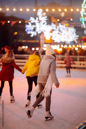 Young woman ice skating on a rink in a Festive Christmas fair in the evening. Smiling woman in winter style clothes skates. Winter holidays concept. Lights around.