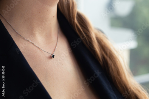 Silver necklace with black stone pendant on woman’s neck, black blazer, elegant style. close-up. Business power woman, successful people, side view