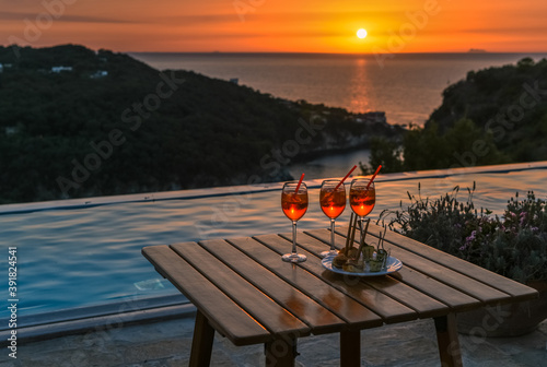 Three glasses of the famous Italian cocktail spritz against the background of pool, sea and sunset