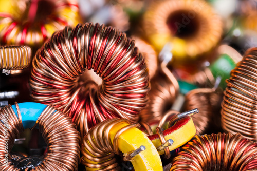 Toroidal electronic inductors on heap in electrotechnical background. Closeup of beautiful induction coils with copper wire winding on magnetic ferrite core. Colored electrical engineering components.