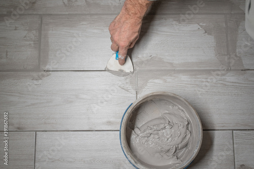 Grouting tiles seams with a rubber trowel. worker applies grout whit rubber trowel tiles