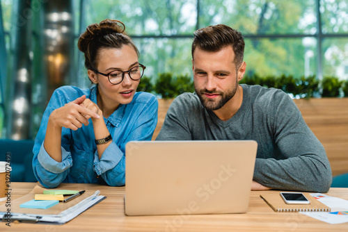 Two young colleagues working together using laptop at office desk