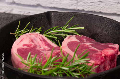 Lamb loin chops with rosemary in a cast iron frying pan. On a black granite and grey brick background