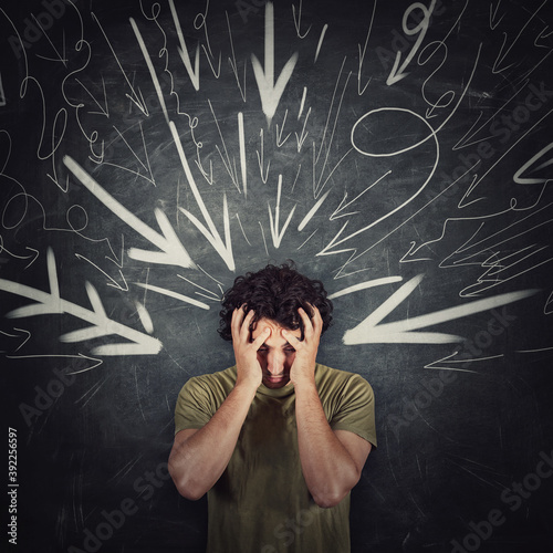 Disappointed guy covers face with his hands, looking down introverted and depressed, being under pressure as multiple arrows points tension negativity to his head. Person suffering emotional breakdown