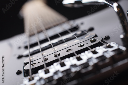 Elegant electric guitar on black background close up point of view from bridge to neck focused on bridge and humbucker pickups with silver tremolo