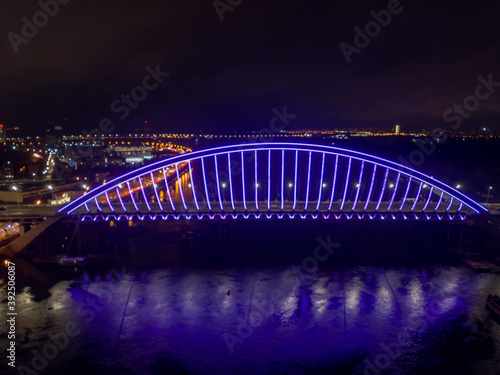 Aerial drone view. Modern arch cable-stayed bridge in Kiev in the evening. Colored lighting of the arch of the bridge.