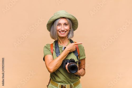 middle age woman smiling cheerfully, feeling happy and pointing to the side and upwards, showing object in copy space