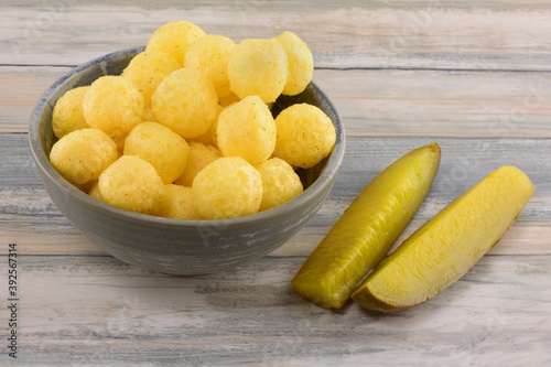Dill pickle corn puffs in snack bowl with dill pickle spears in table