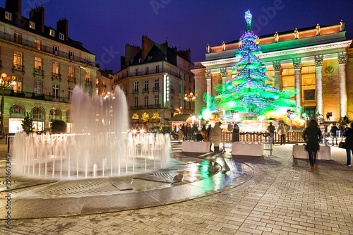 Festivités de Noël sur la place d'une ville en hiver, avec jets d'eau et manège en forme de sapin géant. Place Graslin, Nantes