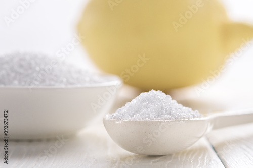 Spoon with citric acid and lemon on a white wooden table.