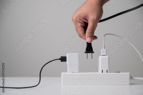 Hand holding Electric plug put on multiple socket. Electrical equipment, electrical wires and power strips in the house. Earth Hour saving electrical energy.