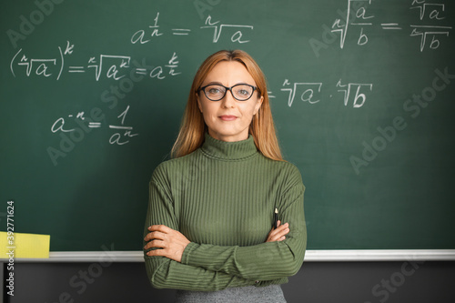 Mature maths teacher near blackboard in classroom