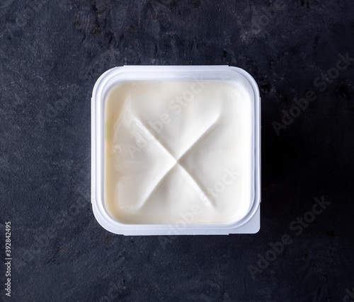 White yogurt in plastic square cup on gray background. Flat view.