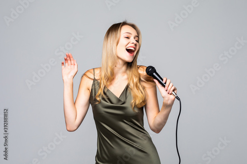 Portrait of female singer wearing evening dress and keeping microphone on grey background. Concept of music